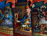 26 Trugo Gompa Statues Of Guhyasamaja Akshobhyavajra, Padmasambhava And Chakrasamvara Trugo Gompa has statues of Guhyasamaja Akshobhyavajra, Padmasambhava (Tib. Guru Rinpoche), and Chakrasamvara. The left statue is dark blue Guhyasamaja Akshobhyavajra in yab yum with his consort who is light blue. Gurla Mandhata in Western Tibet is considered to be his paradise. Guhyasamaja is dark blue in colour as distinct from the light blue complexion of his consort, with two hands crossed against the breast holding a vajra and ghanta bell, his upper right and left hands holding a chakra wheel and flaming jewel, and his two lower hands holding a lotus and sword. His consort has three faces: red, light blue, and white. Her original hands embrace the yab at the back, the upper hands hold the flaming mani jewel and chakra wheel while the lower ones carry the sword of wisdom and lotus. The dark blue right statue on the right is Chakrasamvara with his red consort Vajravarahi (Tib.: Dorje Pagmo). His two central hands embrace his consort and hold a vajra and bell. His right hands hold a damaru drum, an axe, a curved chopper and a trident. One of his left hands holds a khatvanga.